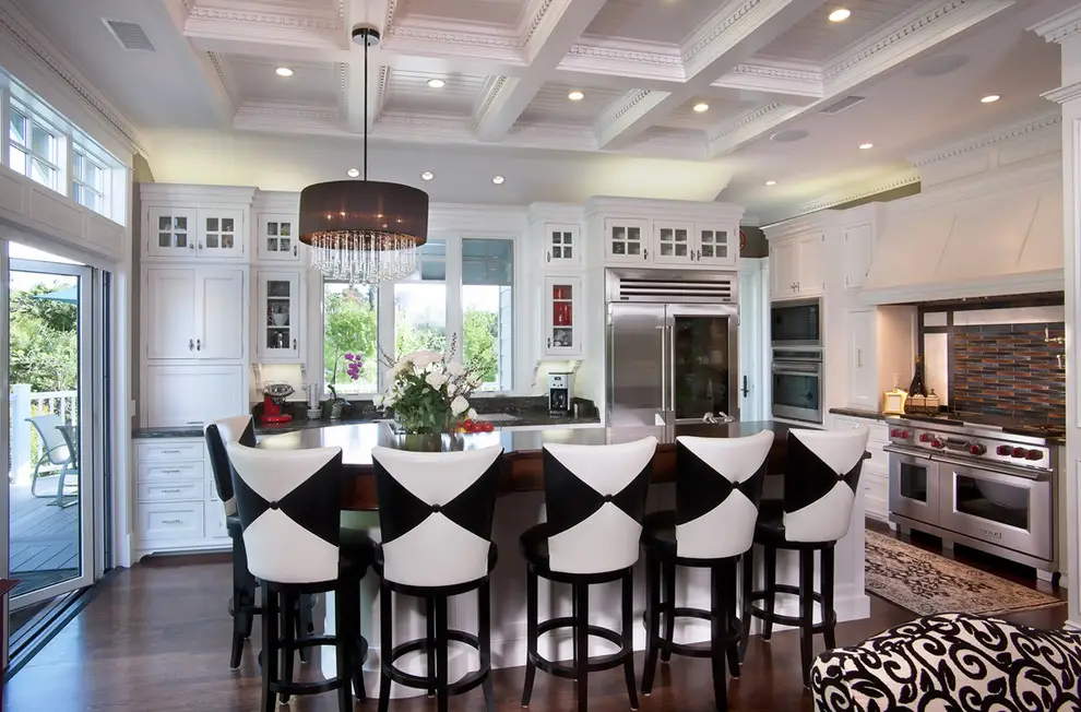 Spacious modern kitchen with white minimalist cabinets and black-and-white bar stools, featuring a center island with flowers, stainless steel appliances, and a chic chandelier.