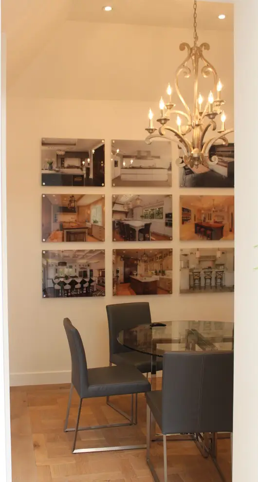 Modern dining area featuring a round glass table with sleek gray chairs and a sophisticated chandelier. The wall displays nine framed images showcasing custom cabinetry and elegant kitchen designs, emphasizing modern kitchen aesthetics and stylish storage solutions.