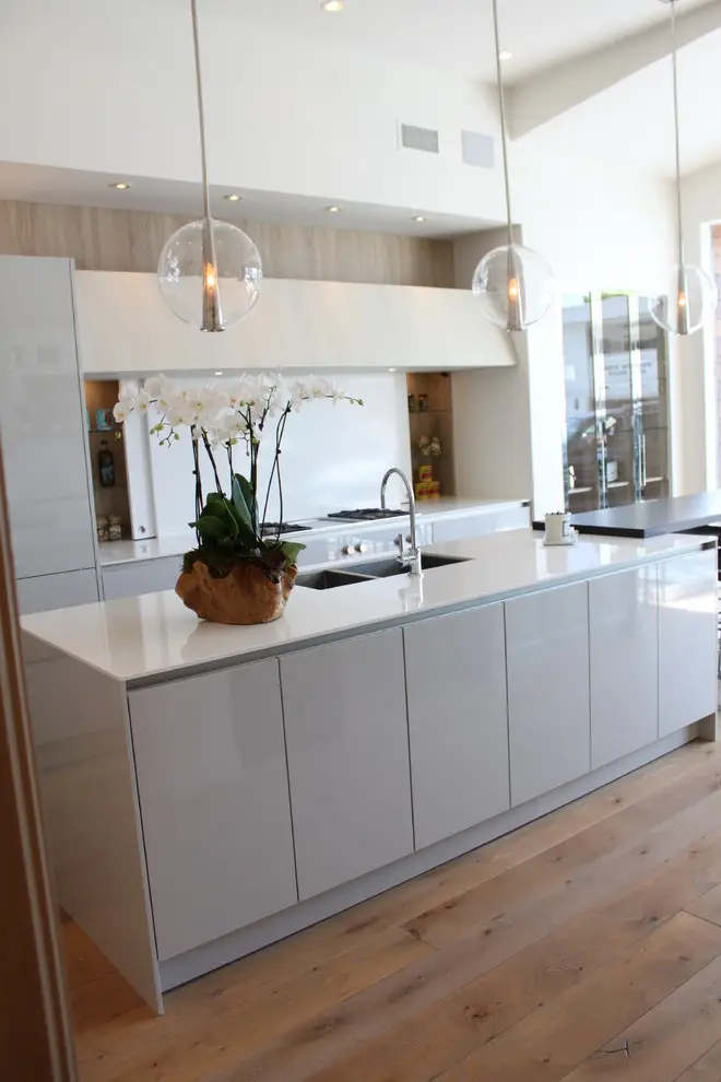 Sleek modern kitchen with custom cabinetry, featuring glossy cabinets and a large island with a white countertop, accented by pendant lights and wood flooring, perfect for elegant storage solutions.