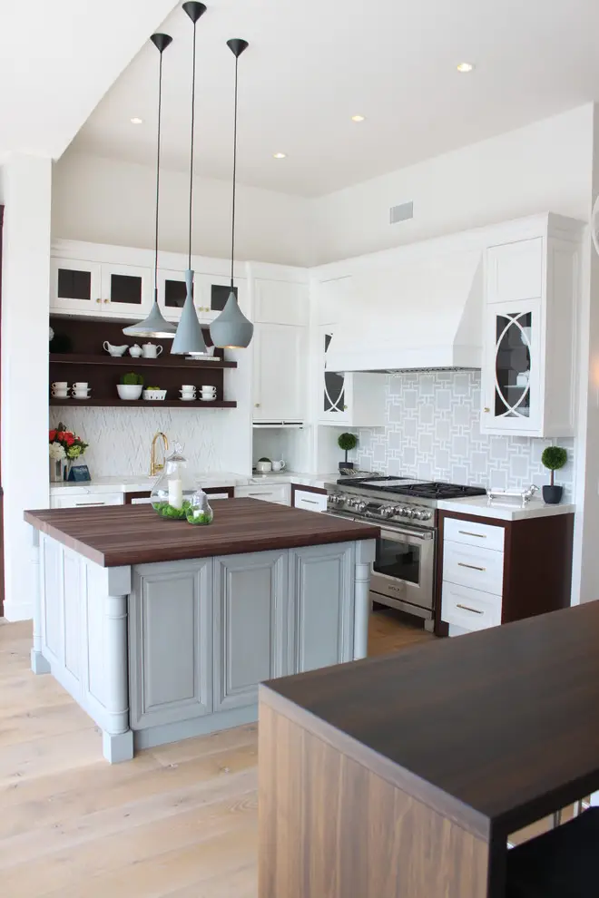 Modern kitchen with custom cabinetry featuring a central island with a dark wooden countertop. Sleek, white cabinets are paired with geometric tile backsplash, open shelves, and contemporary pendant lights for an elegant storage solution.
