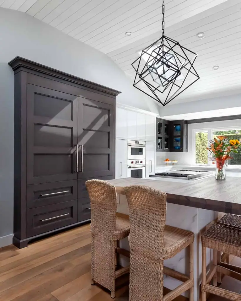 Modern kitchen with custom cabinetry in La Jolla, featuring dark wood cabinets, a light wooden island, rattan bar stools, and a geometric pendant light. Premium design elements and ample storage solutions are highlighted.