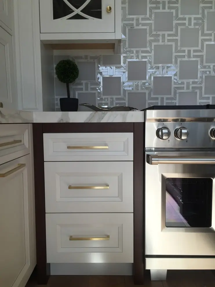 Modern kitchen featuring custom cabinetry with white and dark wood finishes, elegant gold handles, and a stainless steel oven. The backsplash showcases a geometric pattern, adding a contemporary touch to the kitchen design.