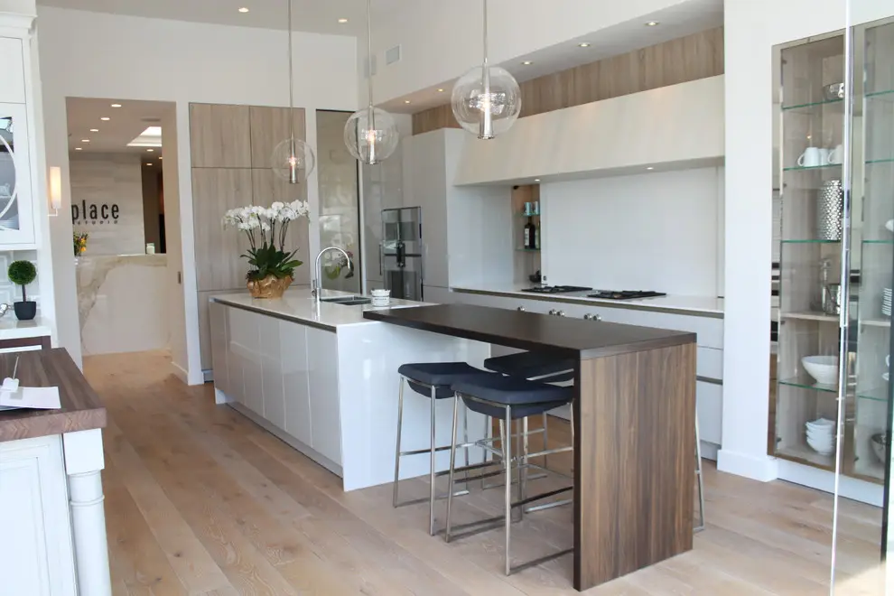 Modern kitchen with custom cabinetry, featuring sleek white cabinets, wood accents, pendant lighting, and a functional island with seating. Elegant storage solutions are displayed, enhancing the contemporary design.