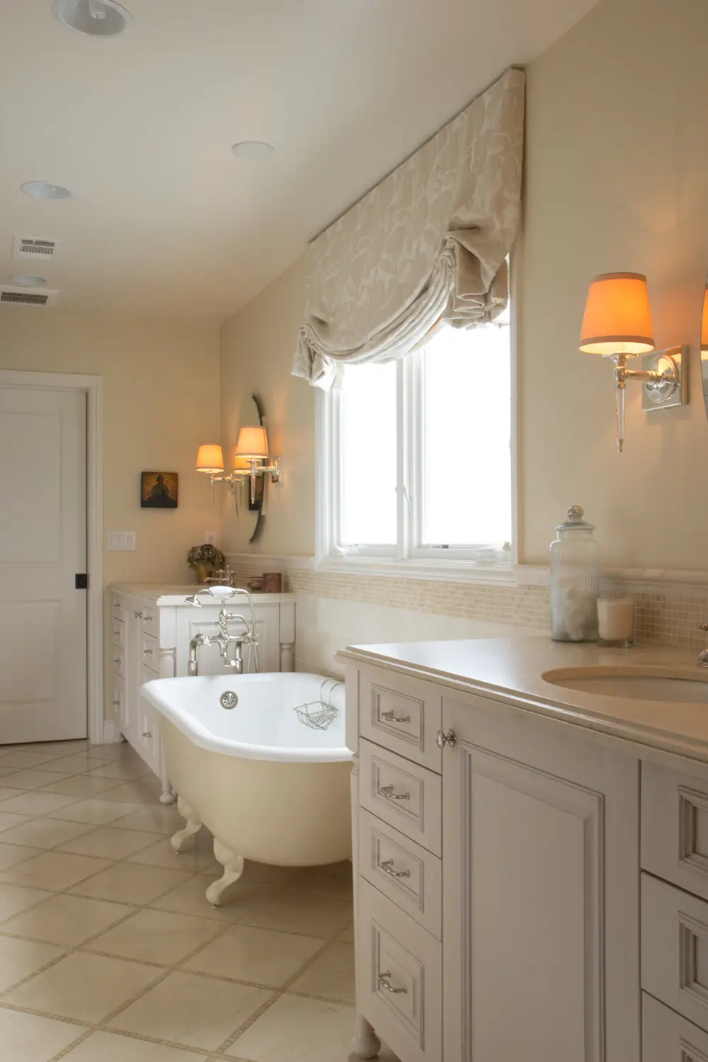 Elegant bathroom featuring a freestanding clawfoot bathtub, custom cabinetry with ornate handles, and a vanity with a marble countertop. Warm lighting from
