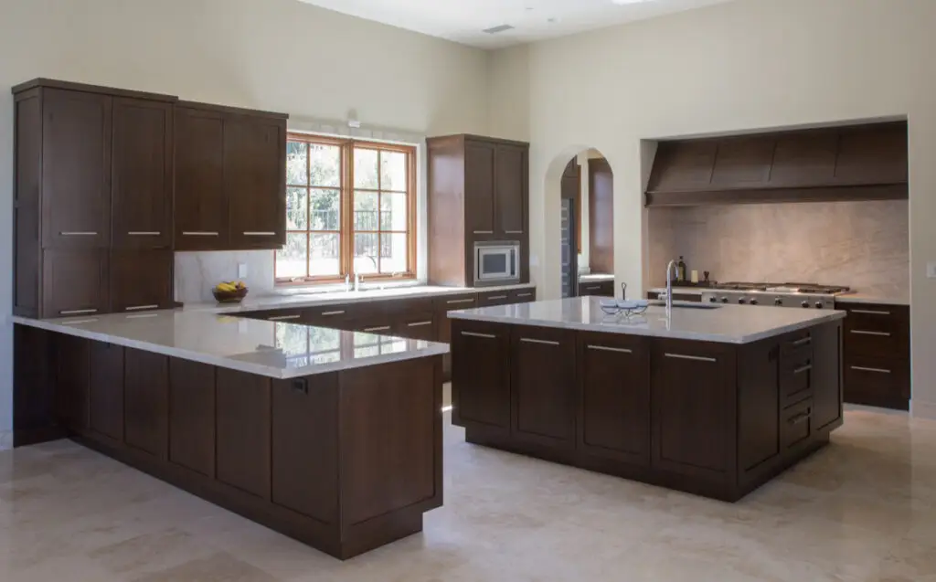 Spacious modern kitchen with dark wood custom cabinets and drawers, featuring a large center island with a marble countertop, stainless steel appliances, and ample natural light from a window.