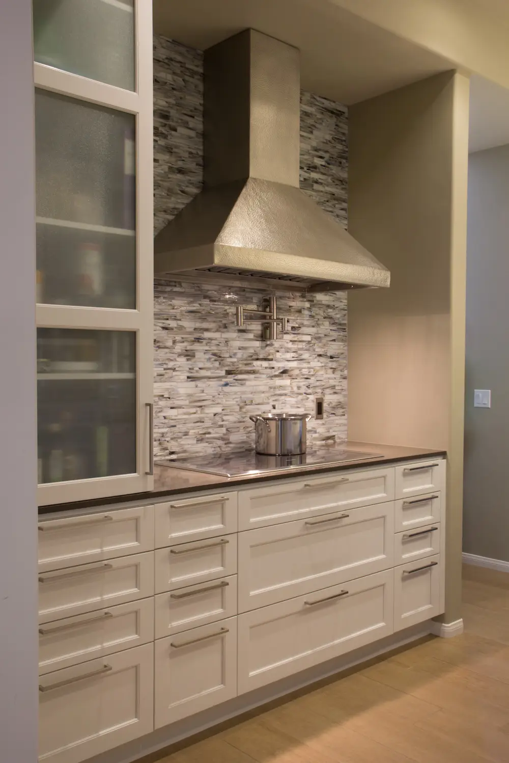 Modern kitchen with custom cabinetry featuring white drawers and cabinets, a sleek stainless steel range hood, and a textured stone backsplash. Ideal for modern kitchen design and storage solutions.