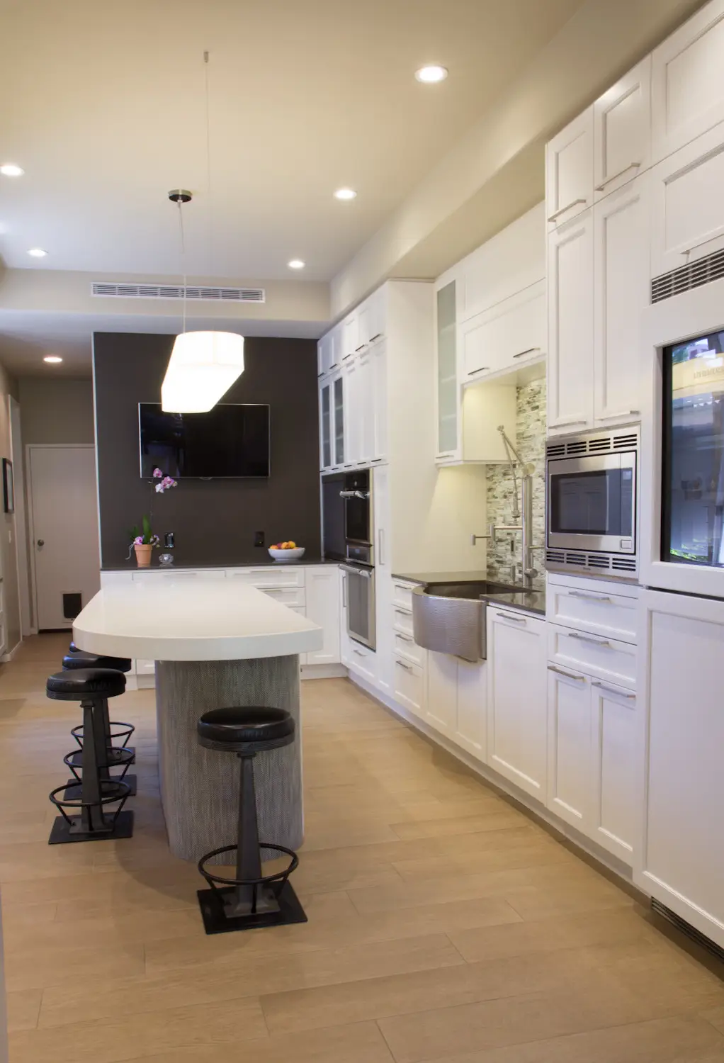 Modern kitchen with custom cabinetry featuring sleek white cabinets, integrated appliances, a kitchen island with bar stools, and contemporary lighting fixtures for efficient storage solutions.