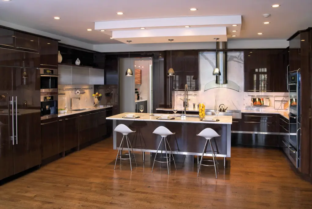 Modern kitchen design with custom dark wood cabinets, a large central island with white countertops, and three white bar stools, featuring state-of-the-art appliances and elegant lighting fixtures in a spacious setting by Inplace Studio.