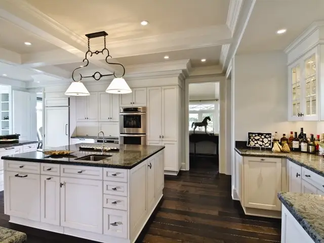 Modern kitchen interior with custom white cabinetry designed by Inplace Studio, featuring a large island with black granite countertop, elegant pendant lights, and dark wood flooring.