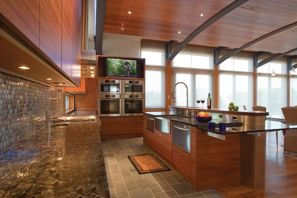 Modern kitchen interior with custom wood cabinets and island by Inplace Studio, featuring stone countertops, metallic backsplash, and a ceiling-mounted TV. Designed for functionality and style, perfect for custom closet and cabinet design.