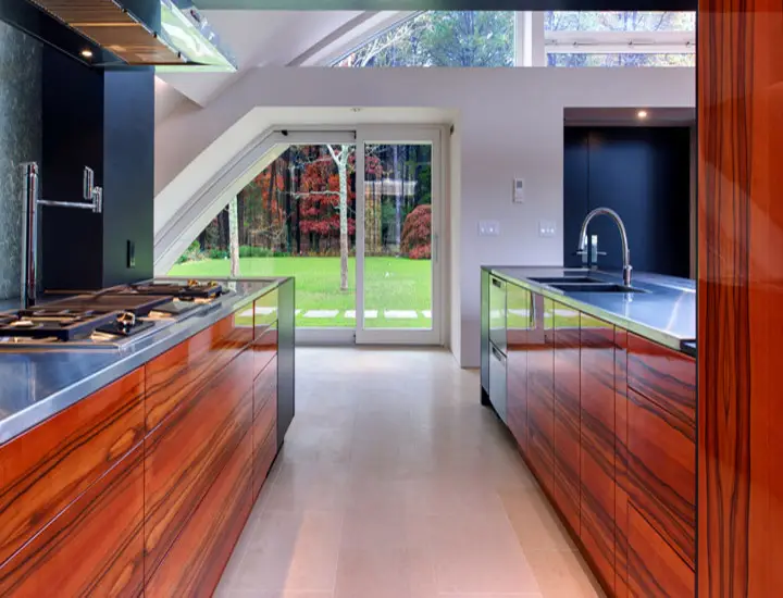 Modern kitchen design featuring custom wood cabinets with sleek metal countertops and large windows showcasing a garden view, highlighting the blend of nature and interior at Inplace Studio.