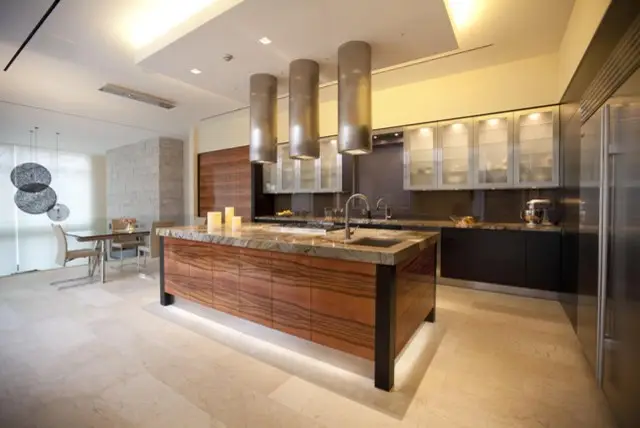 Modern kitchen design by Inplace Studio featuring a spacious island with a marble countertop, sleek wooden cabinets, stainless steel appliances, and unique pendant lighting. The open-concept layout includes a dining area with contemporary furniture, enhancing the space's functionality and style.