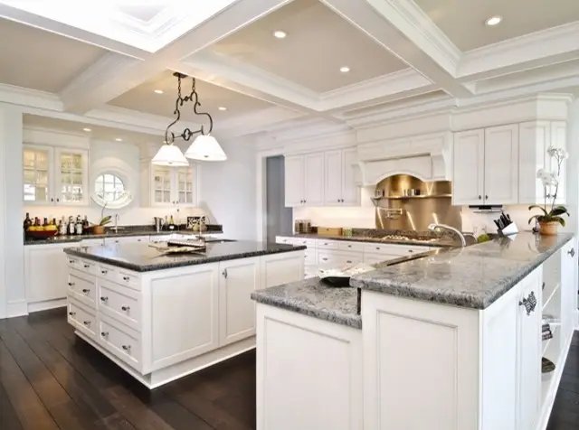 Spacious kitchen featuring custom white cabinets and closets with granite countertops, designed by Inplace Studio. The room is brightened by recessed lighting and elegant pendant lights, highlighting the modern kitchen islands and hardwood flooring.