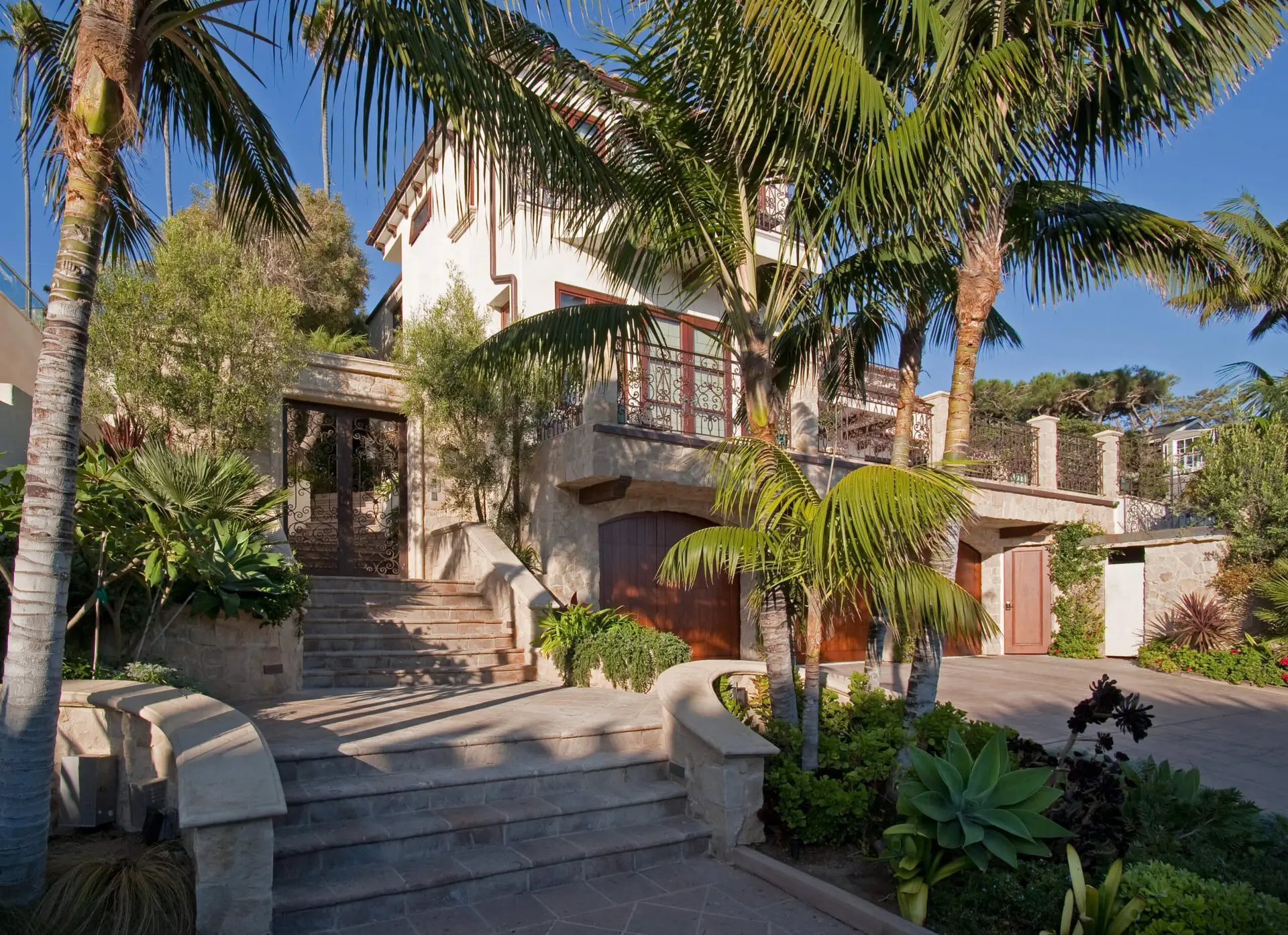 Exterior view of a luxury modern home surrounded by lush greenery and palm trees, featuring custom stonework and elegant architectural details.