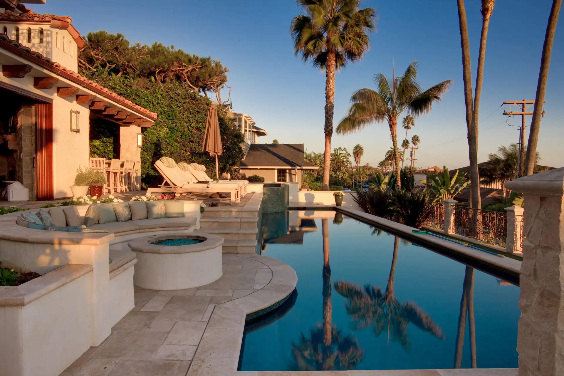Luxury outdoor patio with pool, lounge chairs, and palm trees, showcasing modern home design elements and elegant landscaping at sunset.