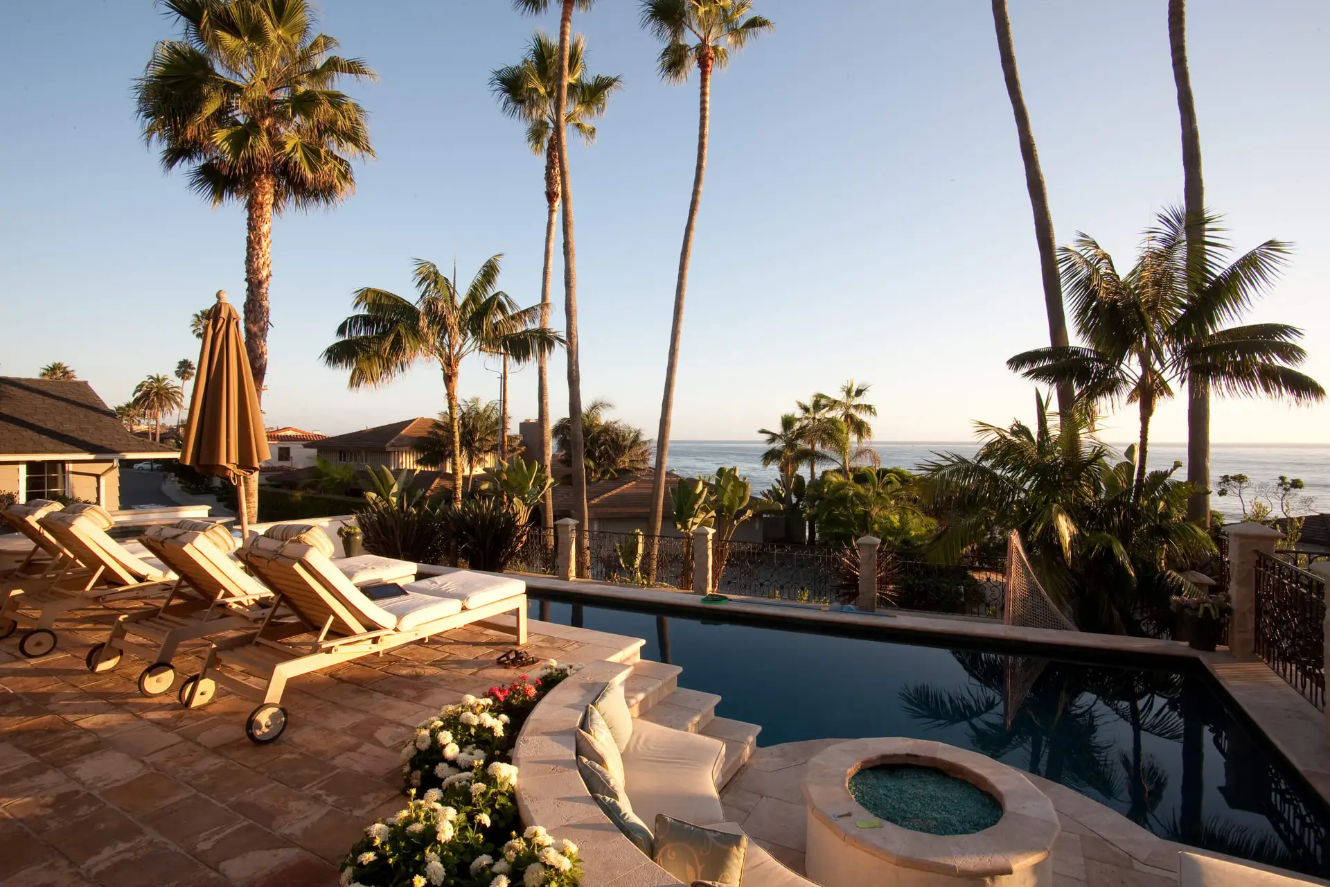 Luxury outdoor patio with modern pool, lounge chairs, and vibrant landscaping featuring palm trees and ocean view, perfect for contemporary homes.