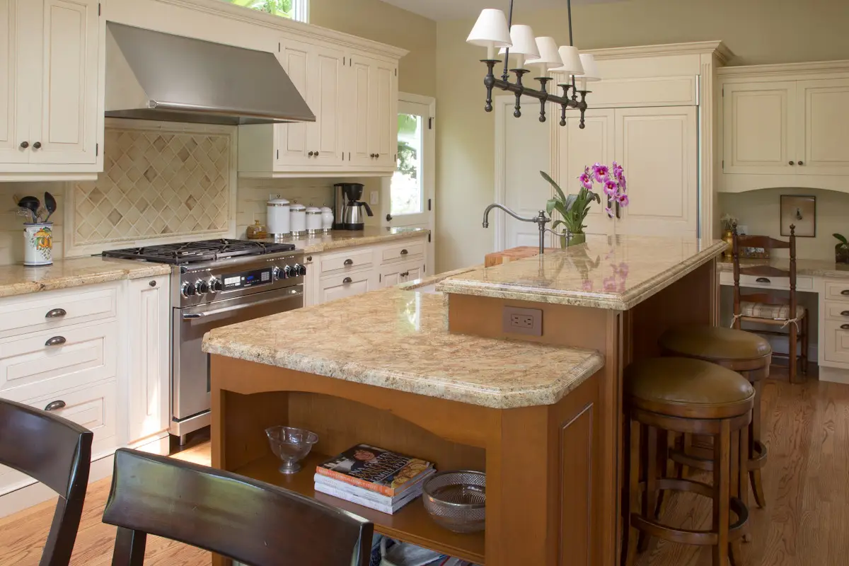 Luxury kitchen with custom beige cabinetry, granite countertops, and an island with stools, featuring stainless steel appliances and elegant lighting for sophisticated design.