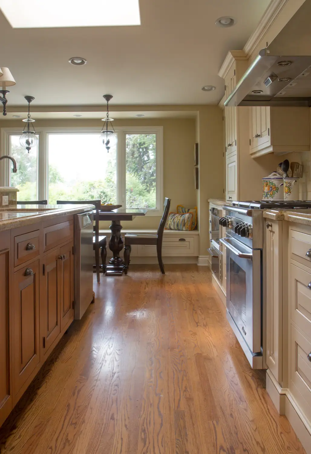 Luxury kitchen interior with custom cabinetry featuring wooden and cream tones, stainless steel appliances, elegant countertops, and a cozy breakfast nook with large windows providing natural light. Design for elegant spaces.