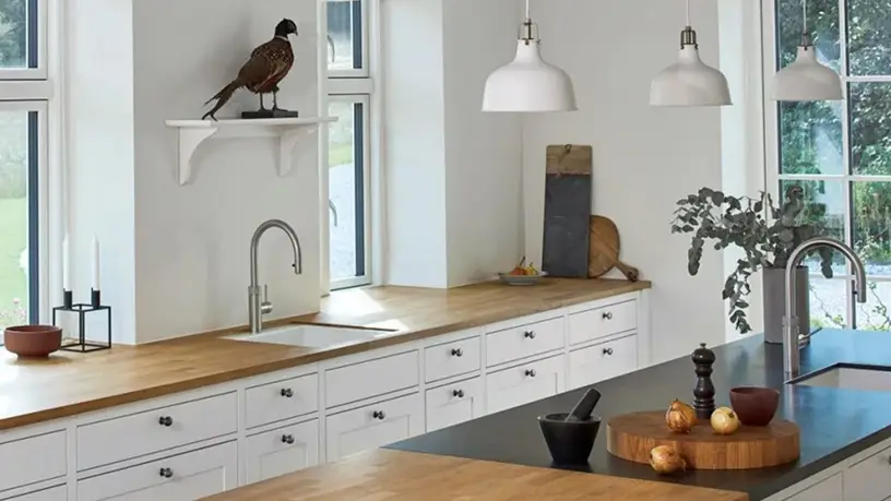 Contemporary kitchen featuring custom white cabinetry and wood countertops, with elegant pendant lighting and a decorative bird statue on a wall shelf. Inplace Studio design.