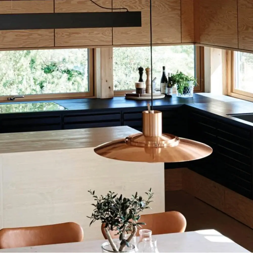 Modern kitchen design featuring custom black cabinetry and light wooden finishes, highlighted by a copper pendant light and large windows offering ample natural light.
