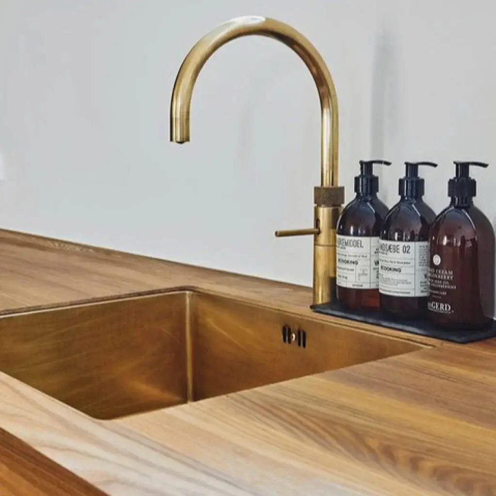 Luxurious modern kitchen sink with sleek brass faucet on wooden countertop, featuring stylish dish soap bottles for a contemporary designer look.