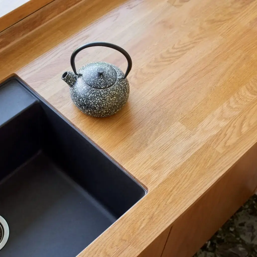 Modern kitchen countertop with a black speckled teapot beside a sleek black sink, showcasing designer kitchen solutions and custom cabinetry by Inplace Studio.