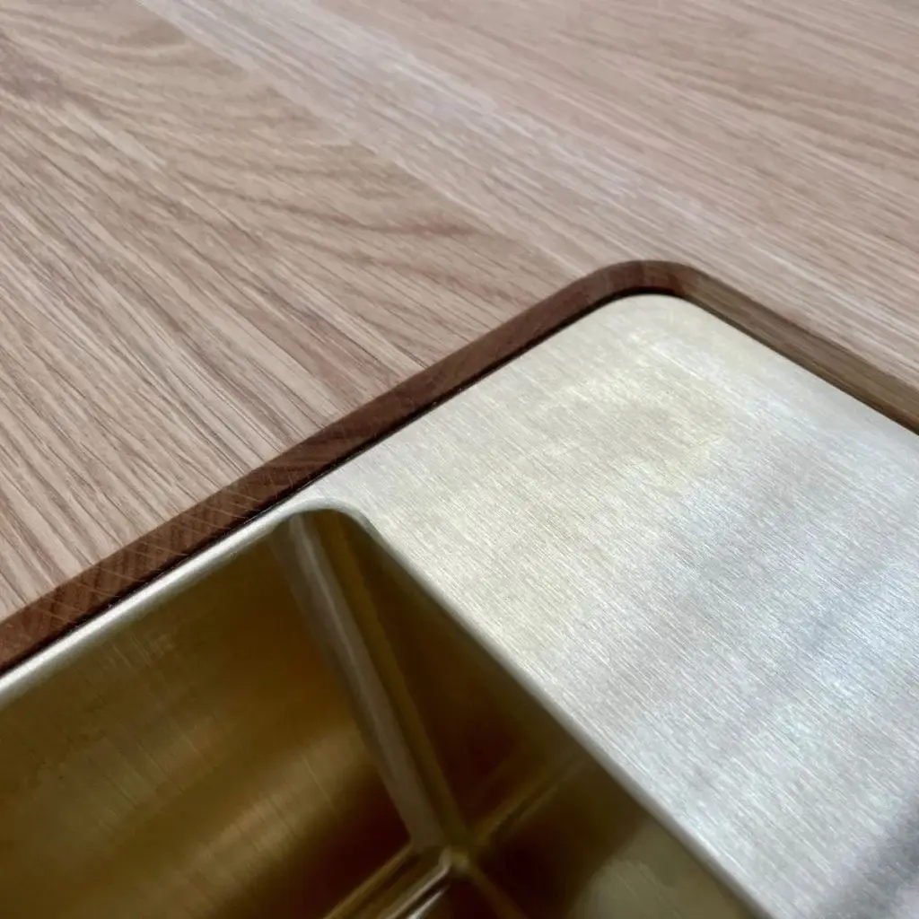 Close-up of a modern kitchen countertop with a sleek metal edge and wooden surface, showcasing high-quality design and craftsmanship in custom cabinetry by Inplace Studio.