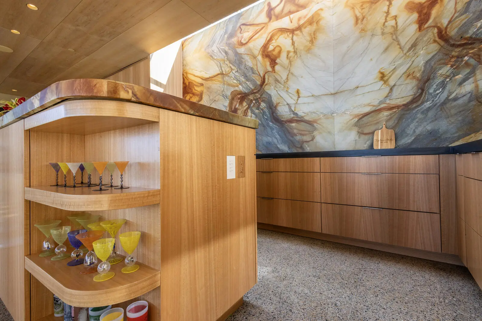Curved eucalyptus veneer island with open display shelving — San Diego custom millwork