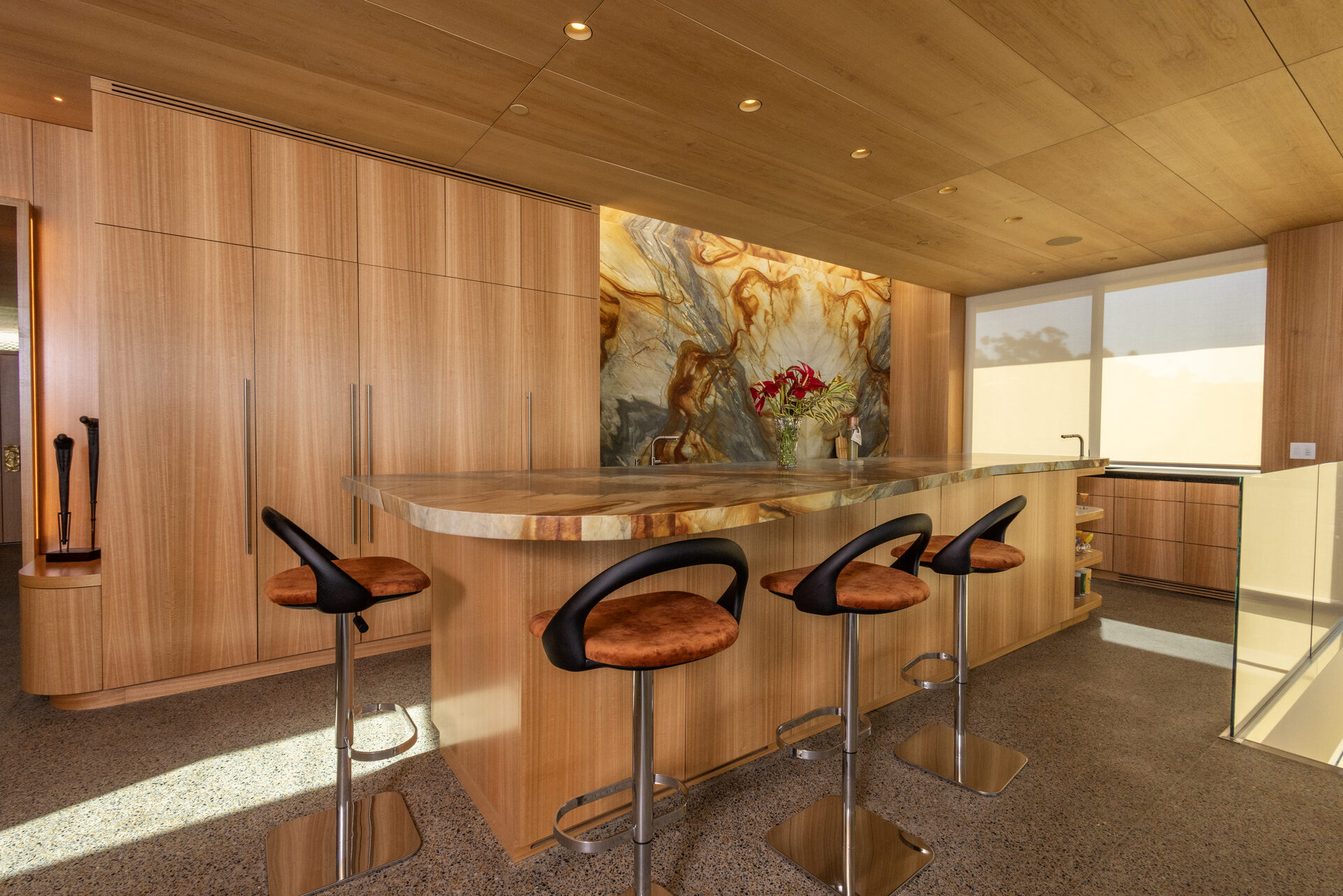 Custom eucalyptus wood veneer bar and curved counter beneath a marble feature wall — San Diego millwork by Inplace Studio