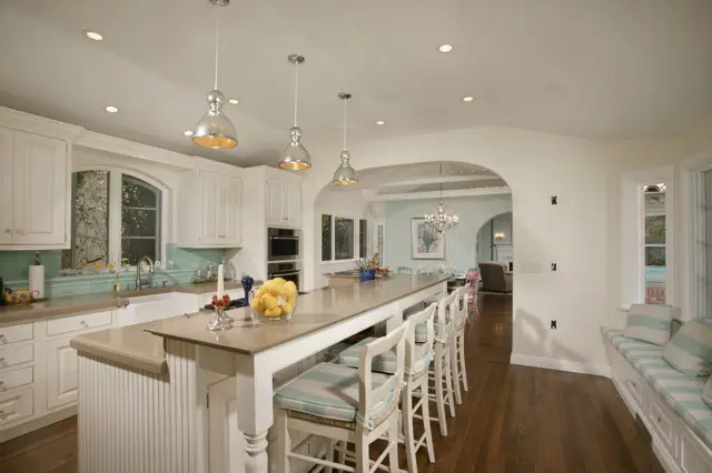 Spacious transitional kitchen with modern design elements featuring a long island with white bar stools, pendant lighting, and mint g