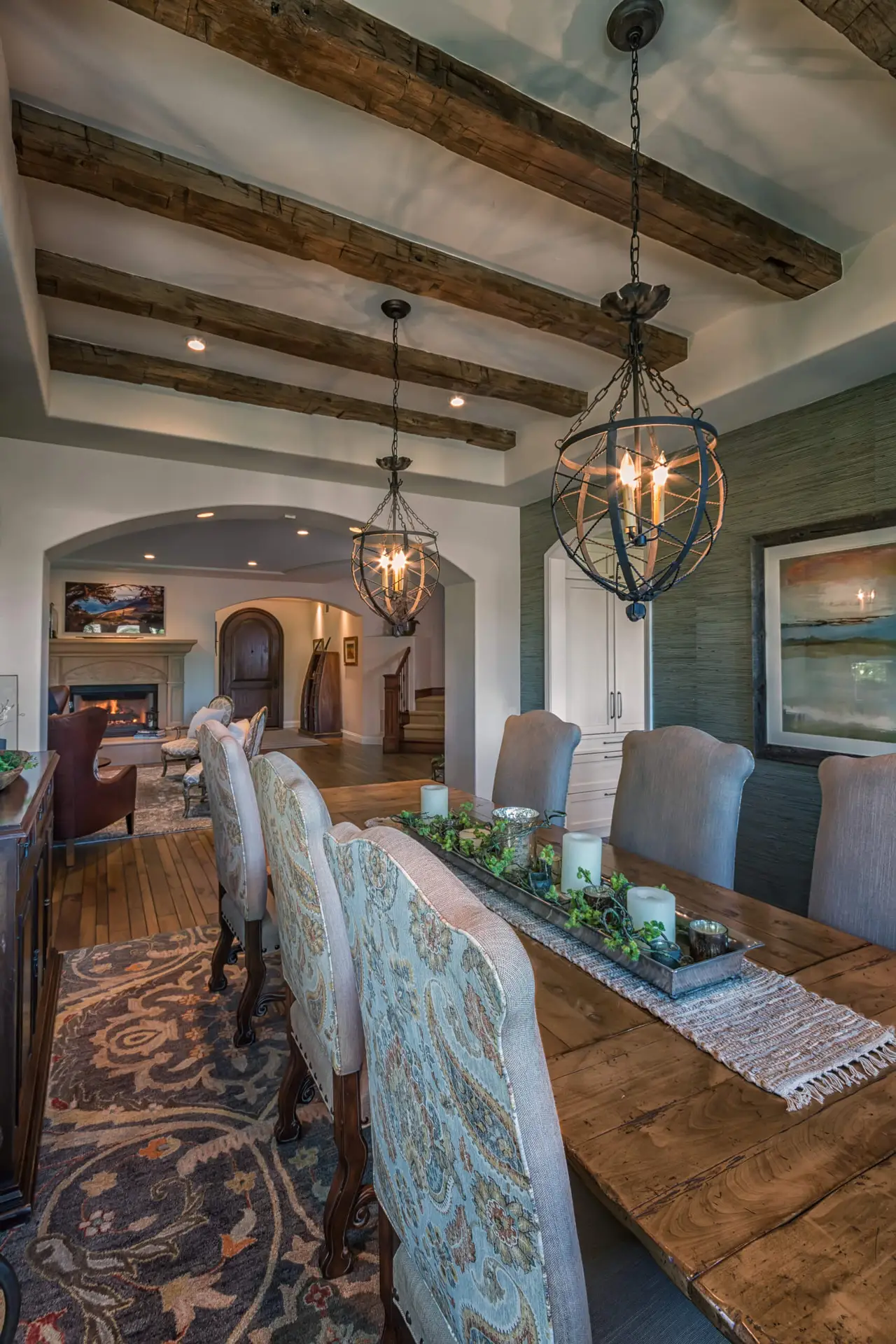 Elegant dining room with wooden beam ceiling, ornate chandeliers, floral-patterned chairs, and a wooden table with greenery centerpiece, exemplifying high-end European-style design in Los Angeles.
