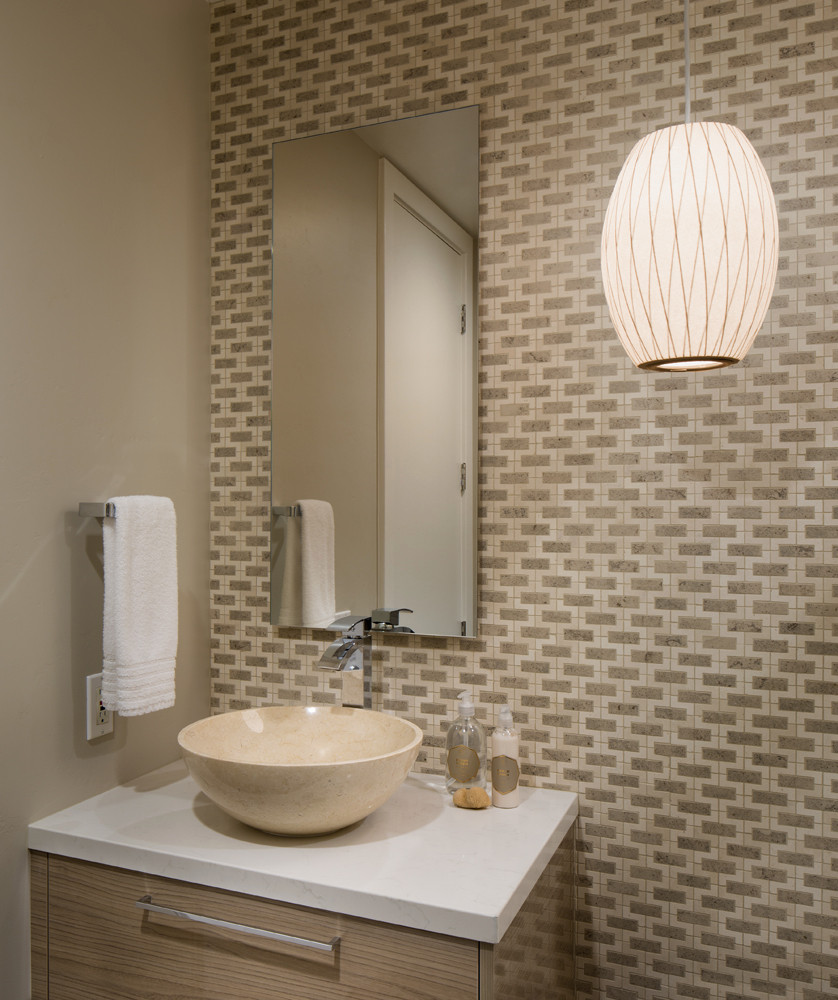 Elegant bathroom design featuring a beige stone vessel sink, modern faucet, and stylish geometric wall tiles, complemented by a light wood vanity and contemporary pendant light.