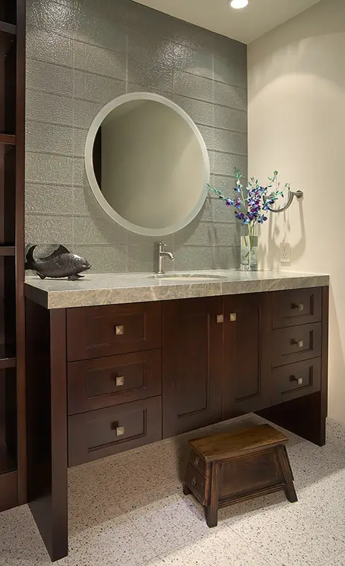 Elegant dark wood bathroom vanity with round mirror and modern faucet on textured wall, showcasing luxury custom cabinets design.