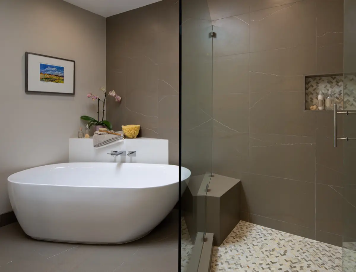Modern bathroom with sleek white freestanding tub, taupe tiles, and elegant shower area.