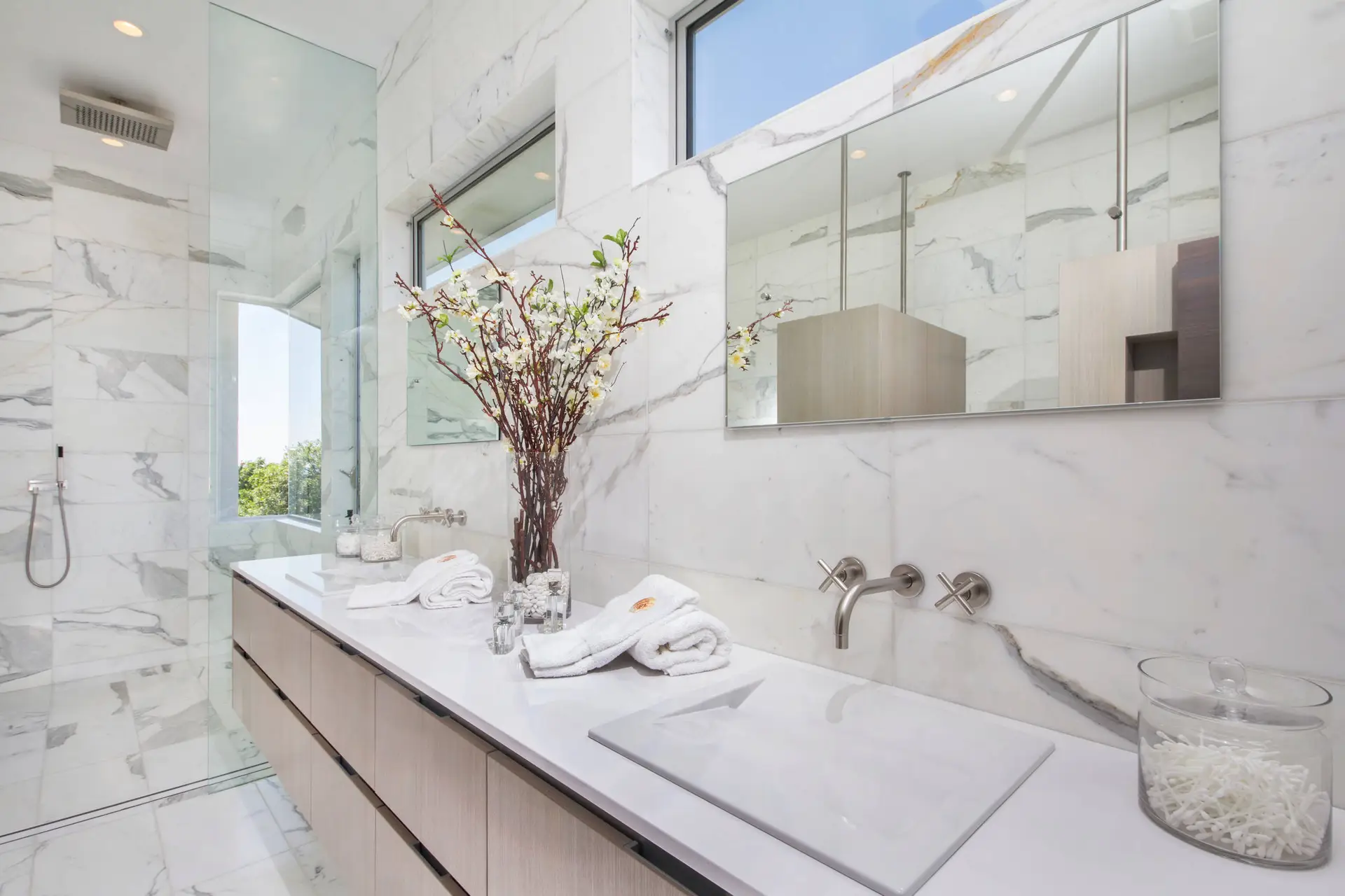 Modern luxury bathroom with white marble walls, custom cabinetry, and a sleek double vanity featuring chrome fixtures and minimalist design.
