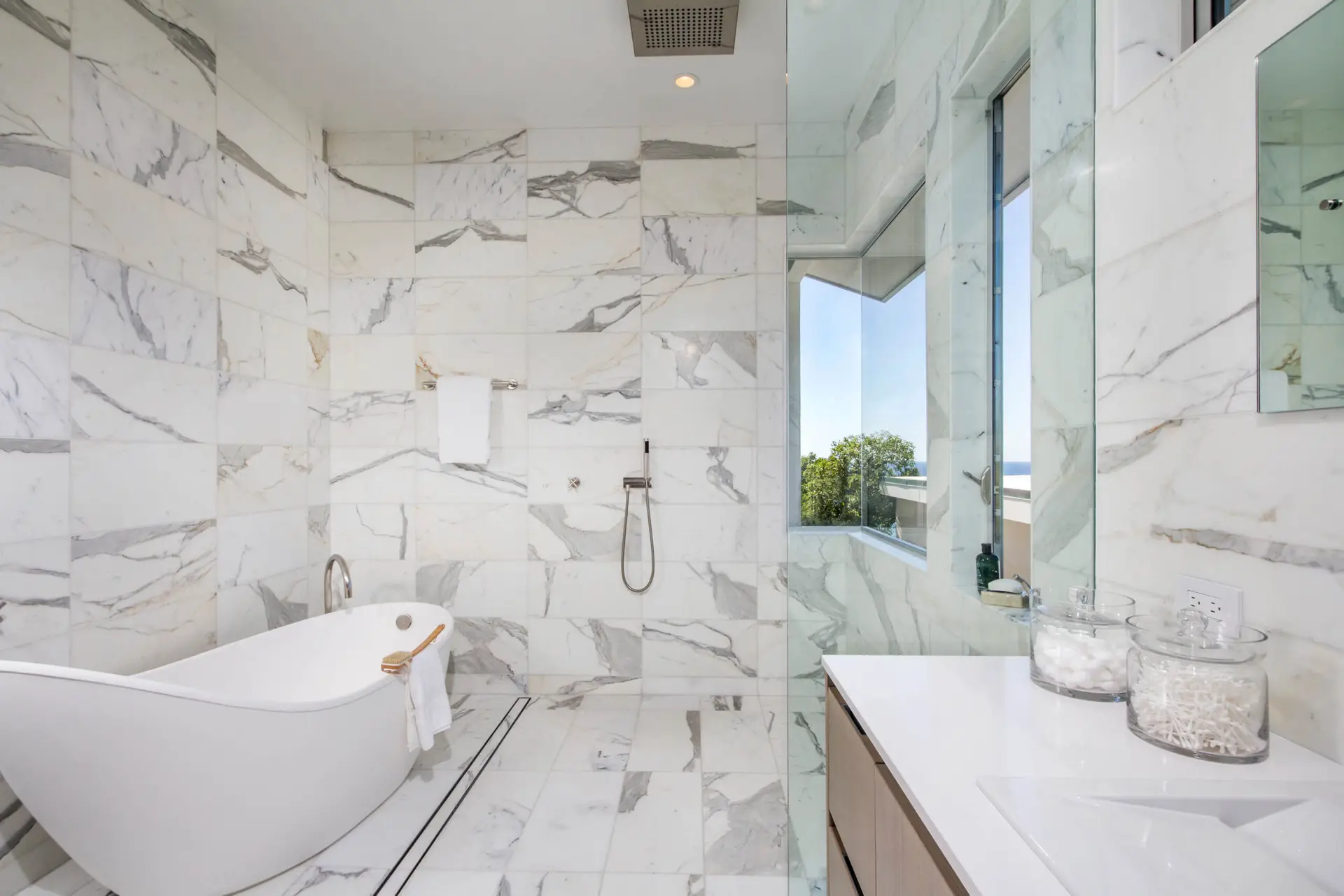 Luxurious marble bathroom featuring a freestanding bathtub, elegant tiles, and a scenic window view, ideal for transforming spaces in Encinitas.