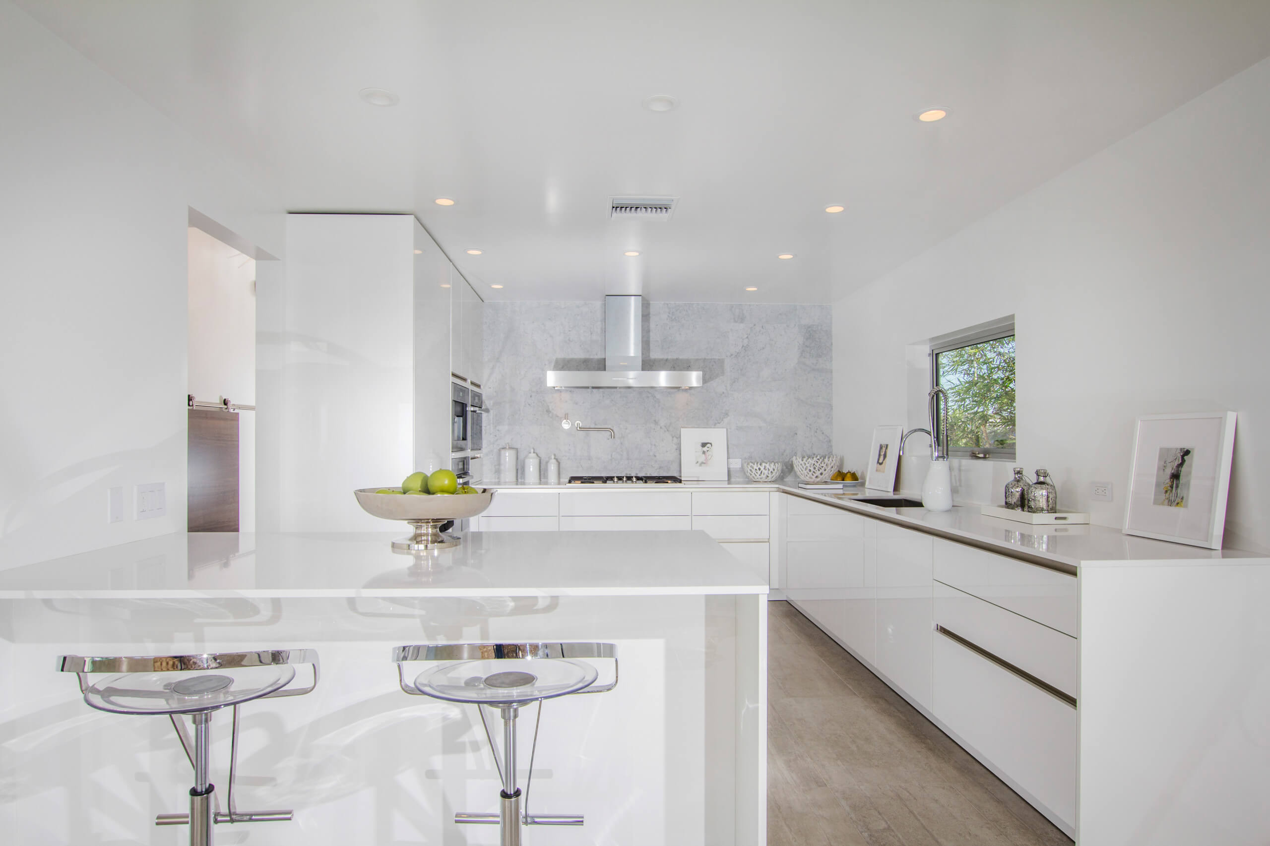 Modern kitchen with sleek custom white cabinets, island with bar stools, and stainless steel appliances in Encinitas. Bright, minimalistic design to enhance space transformation.