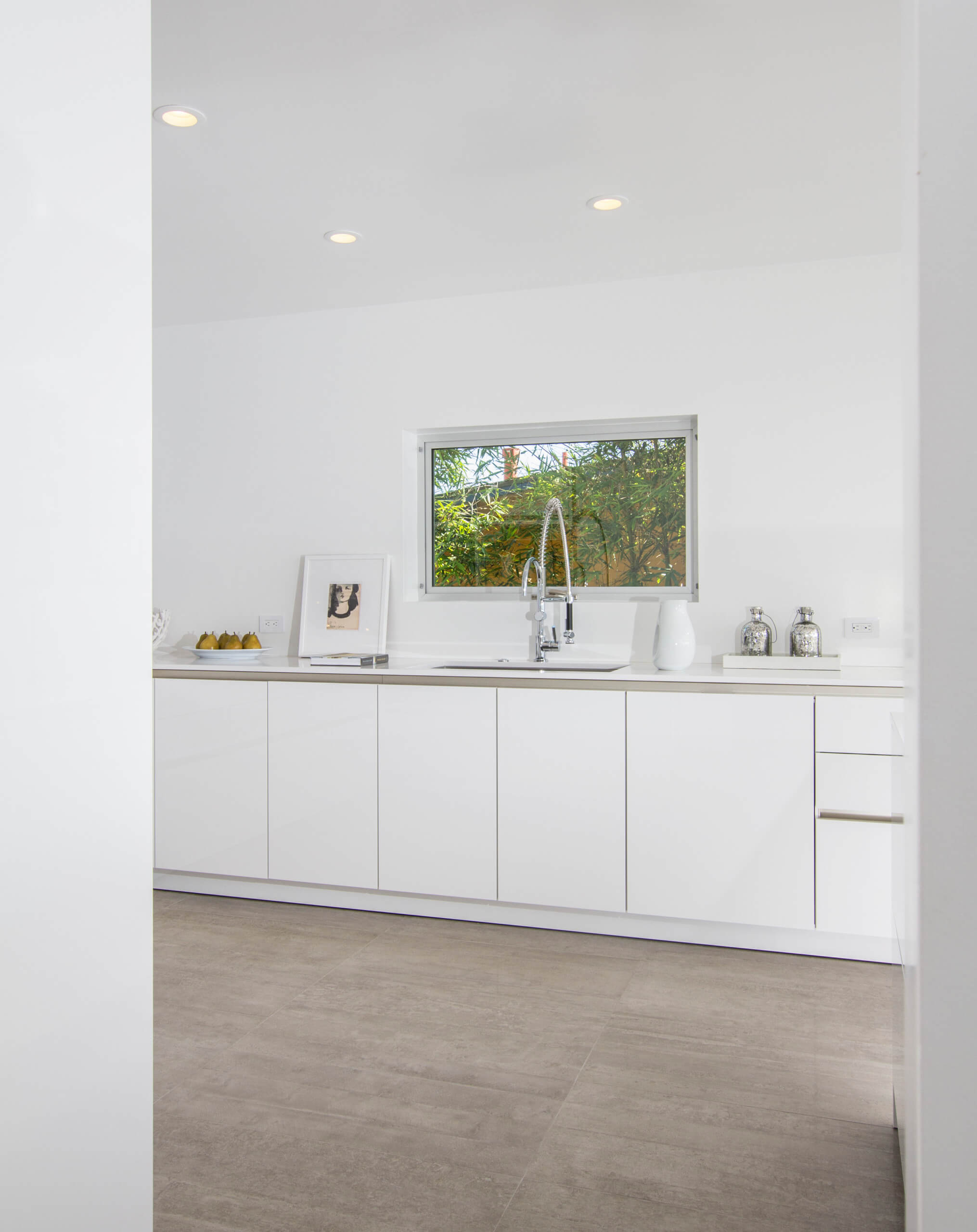Modern white kitchen with sleek custom cabinets and a large window, featuring minimalist decor and a bright, clean aesthetic in Encinitas.