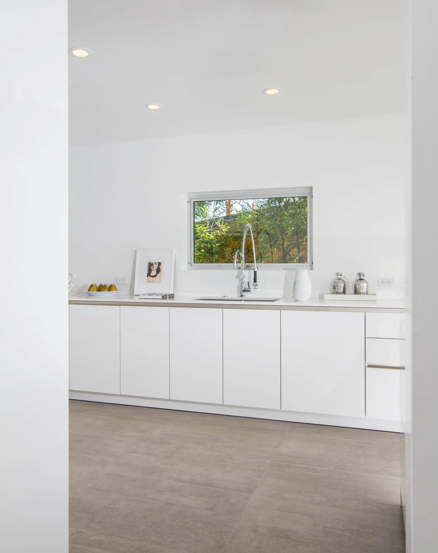 Modern white kitchen with sleek custom cabinets and a large window, featuring minimalist decor and a bright, clean aesthetic in Encinitas.