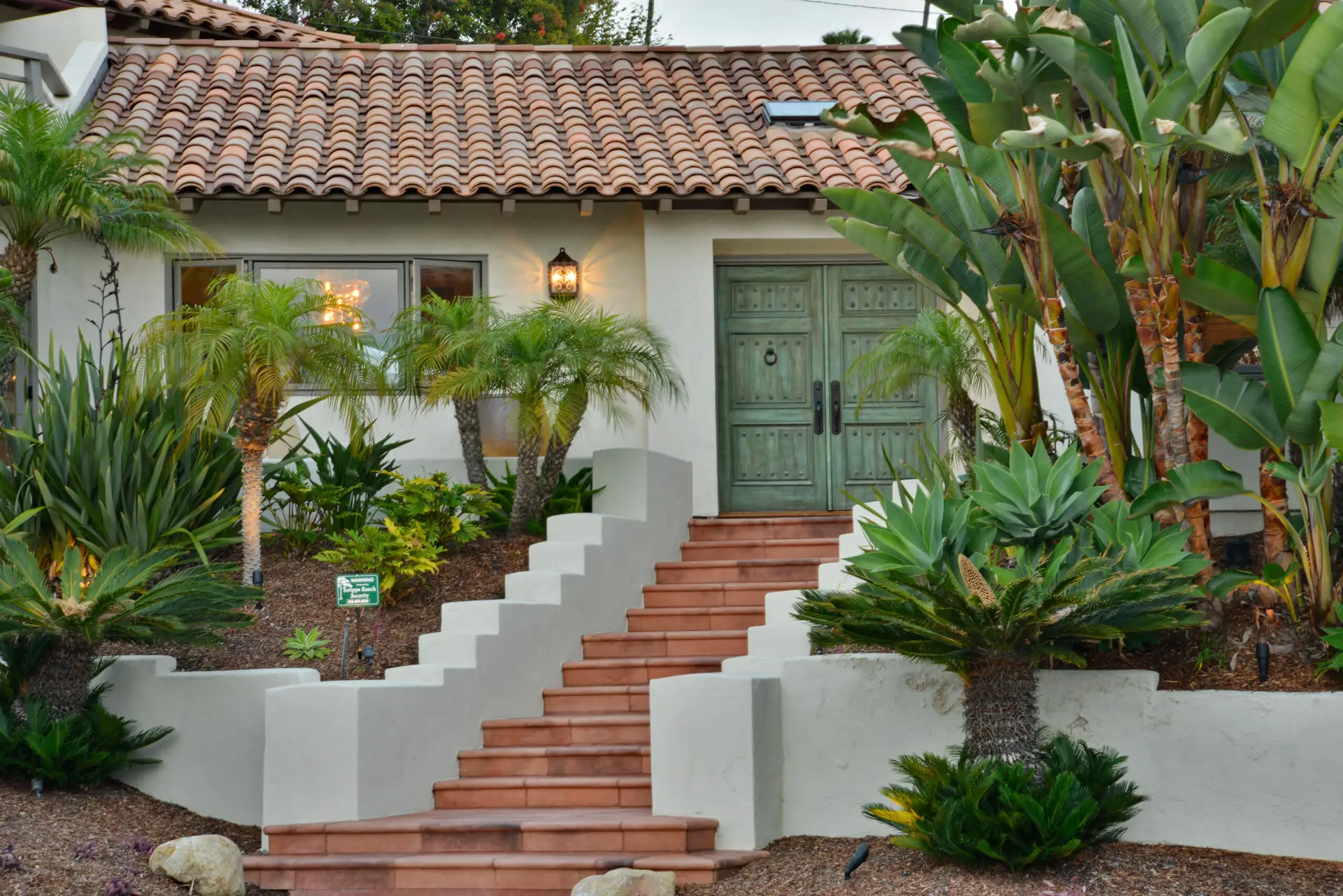 Spanish-style home with terracotta roof tiles, lush landscaping, palm trees