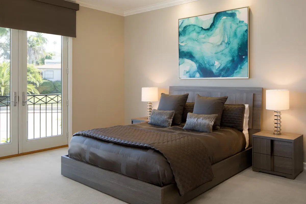 Elegant bedroom with custom cabinetry, featuring a modern grey bed with matching nightstands, stylish lamps, and abstract artwork on the wall, combining function and elegant design.