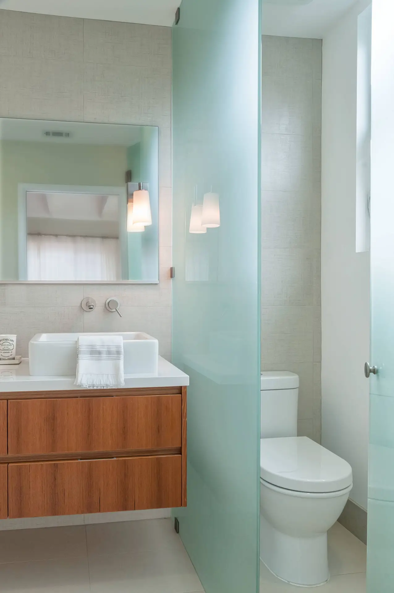 Contemporary bathroom with wooden vanity, modern faucet, and frosted glass partition showcasing an elegant, minimalist design.