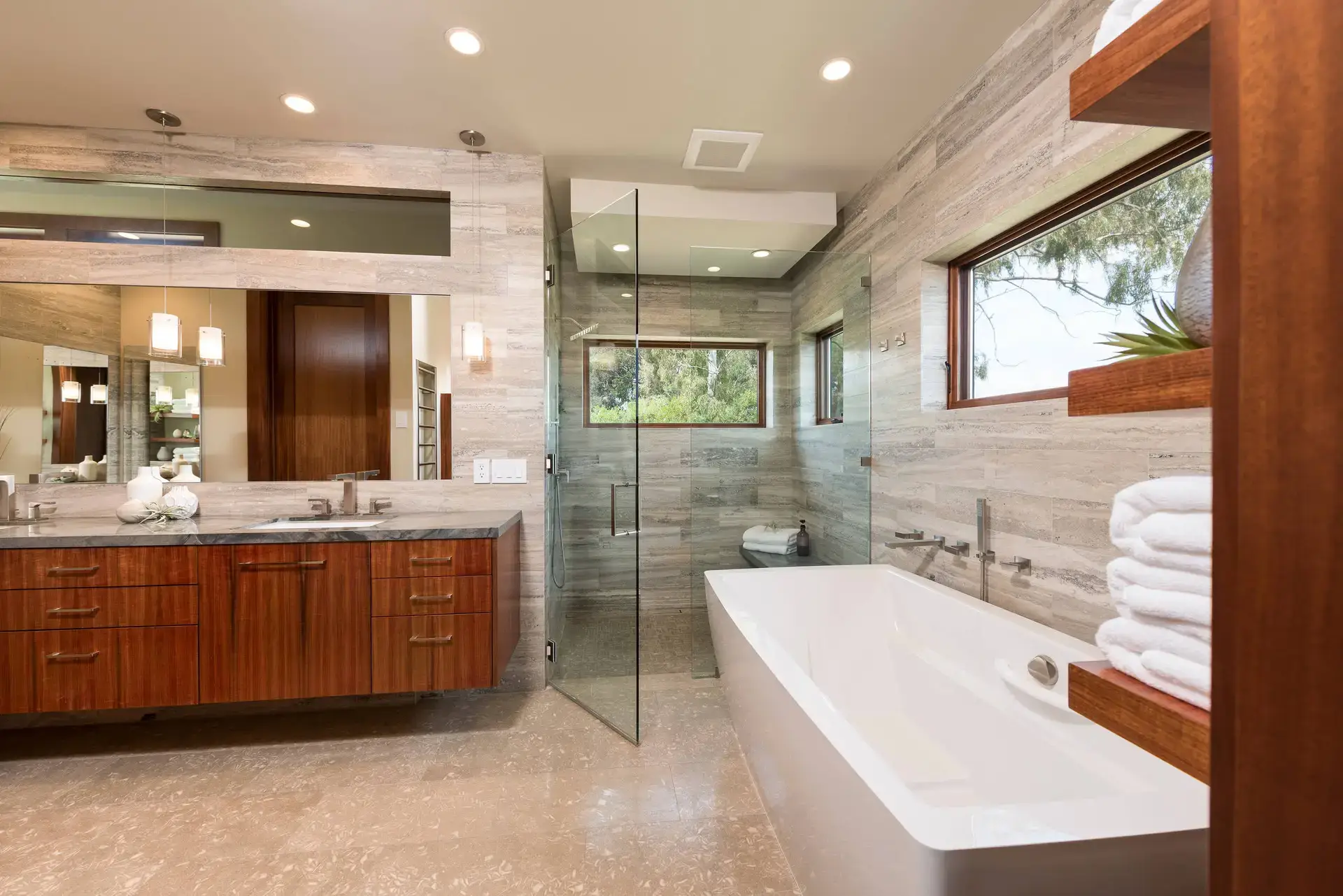 Luxurious bathroom featuring high-end custom wooden cabinetry with a polished countertop in San Diego. Elegant modern shower with glass doors and a large bathtub, complemented by neutral-toned wall tiles and recessed lighting.
