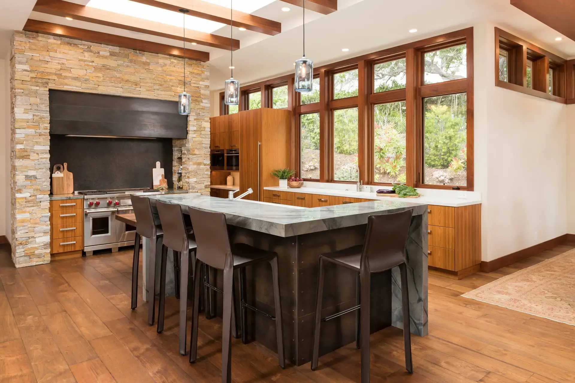 Luxurious custom kitchen with stone brick backsplash, high-end stainless steel appliances, and modern wooden cabinetry located in a San Diego or LA home. Features large windows with natural light and a stylish center island with bar stools.