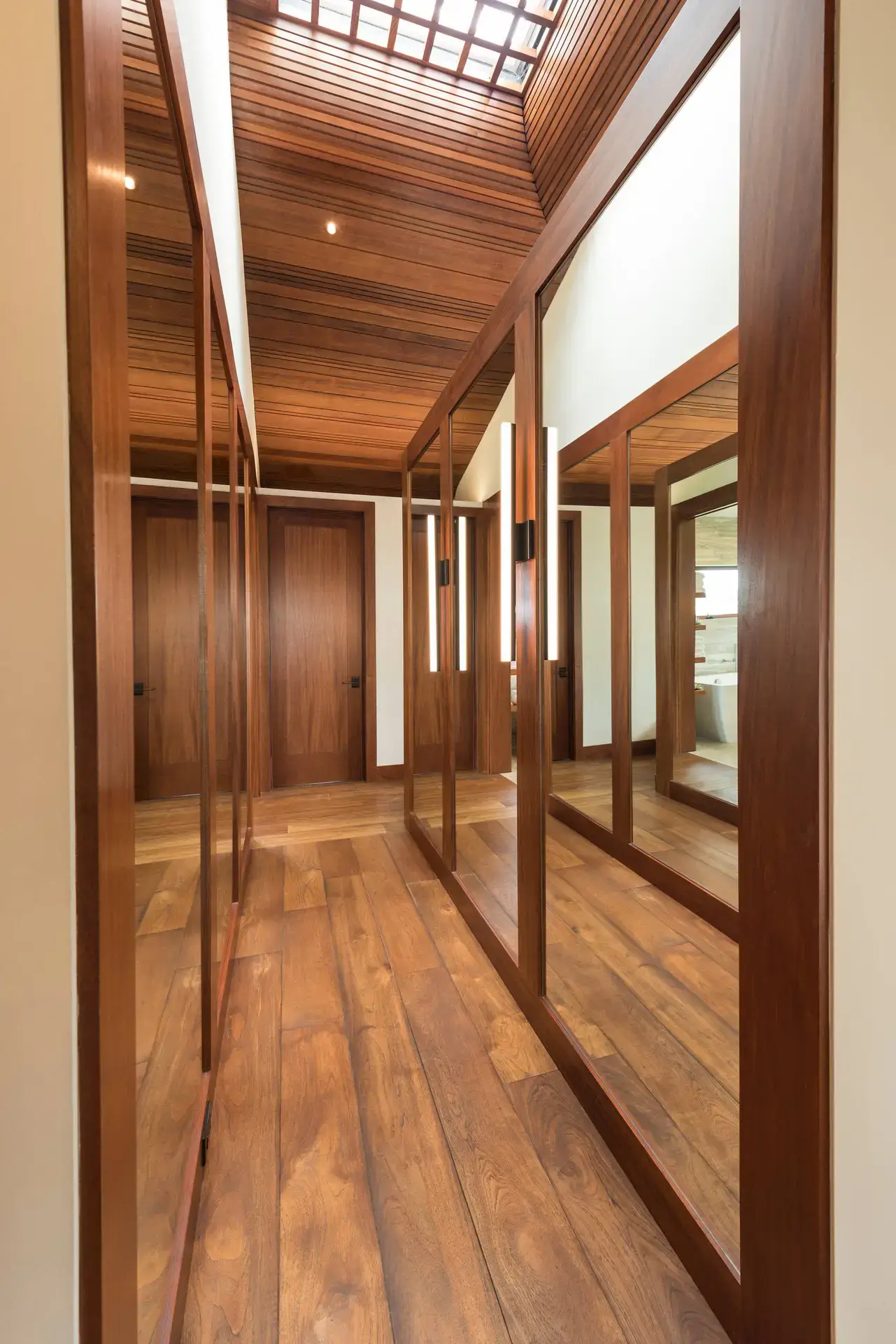 Luxurious custom wood cabinetry in a modern hallway with mirrored panels, featuring rich wood tones and elegant design, showcasing high-end craftsmanship in San Diego and LA.