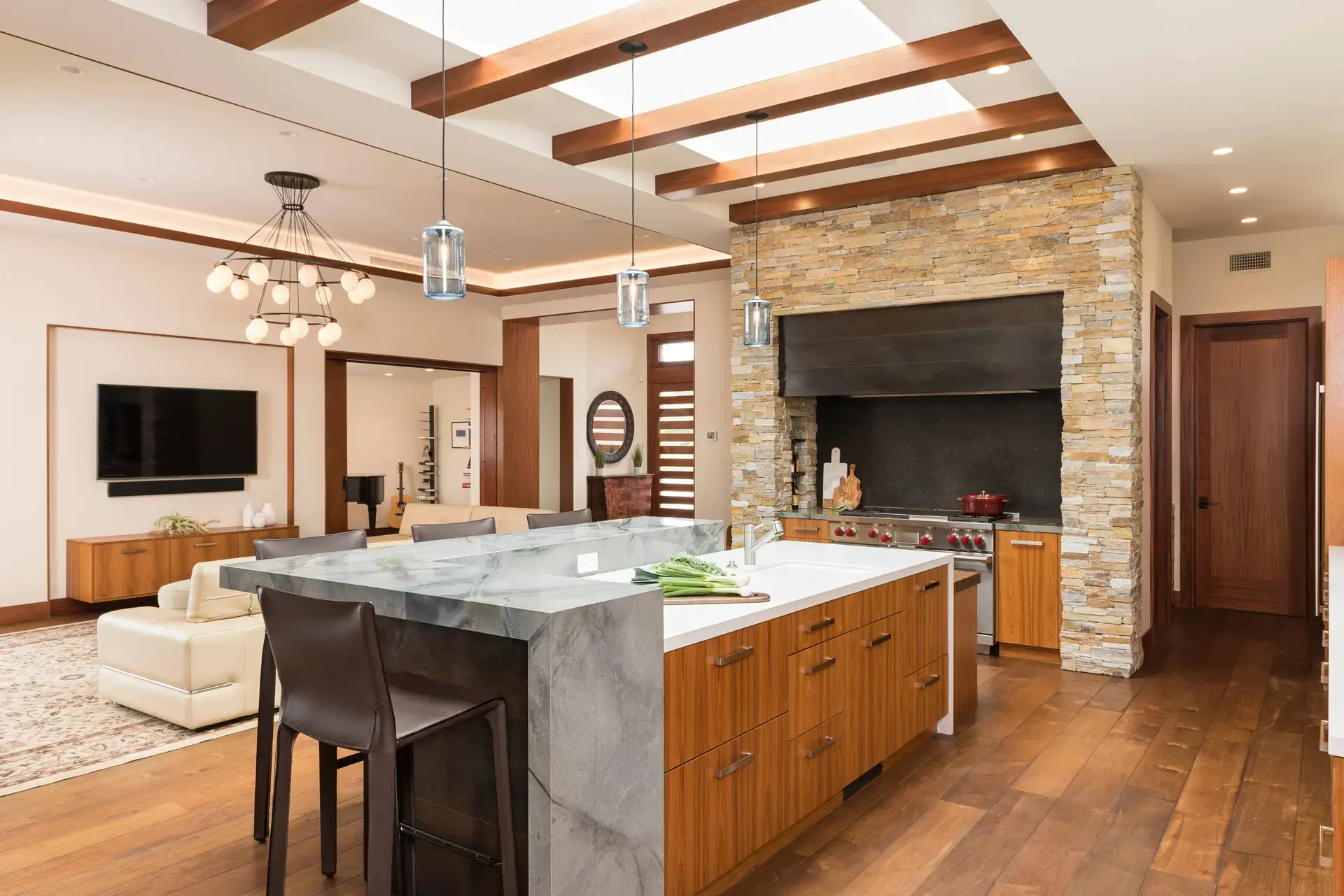Modern kitchen with custom wooden cabinetry, marble island, and stone accent wall, featuring high-end appliances, hardwood floor, and stylish lighting in a luxury home setting.