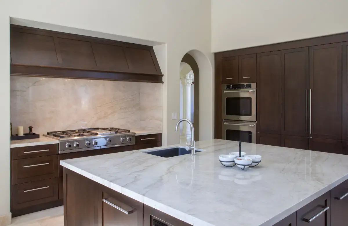 Modern kitchen interior featuring custom storage solutions, sleek wooden cabinetry, and a marble countertop for contemporary living. Stainless steel appliances are integrated seamlessly with dark wood cabinets.