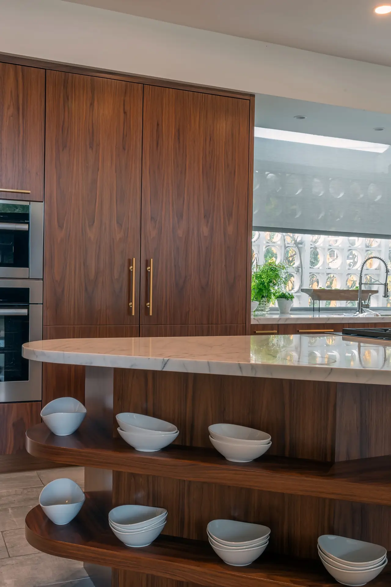 Contemporary kitchen with custom wooden cabinetry, featuring modern stainless steel appliances and a sleek marble countertop. Open shelving displays white bowls, adding a stylish touch to the storage solution.