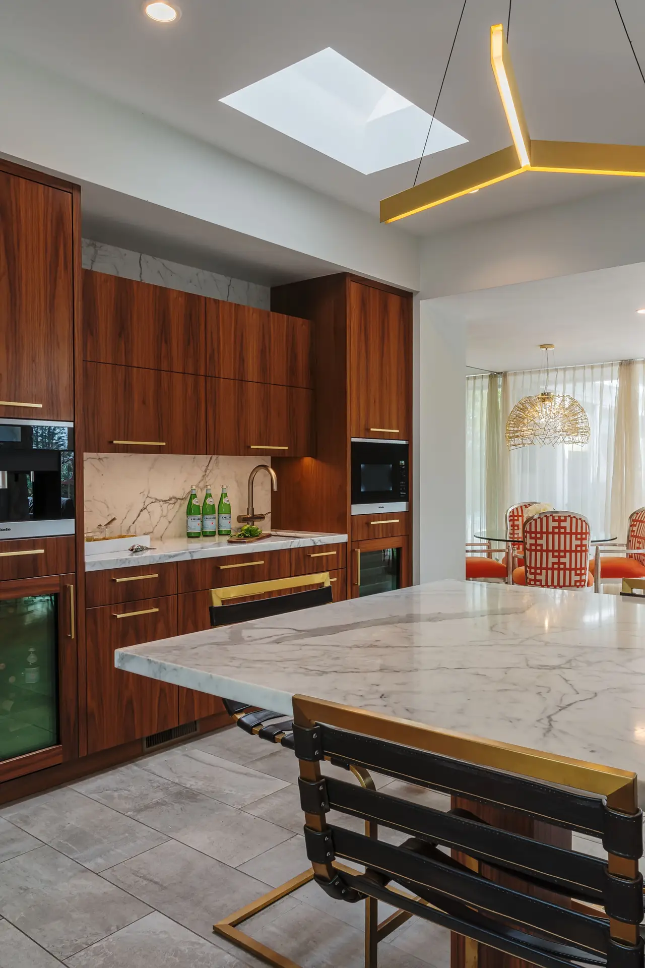 Modern kitchen with custom cabinetry and marble countertops, featuring wooden cabinets, a marble backsplash, and a contemporary black and gold chair design. The image showcases stylish kitchen design and upscale storage solutions.