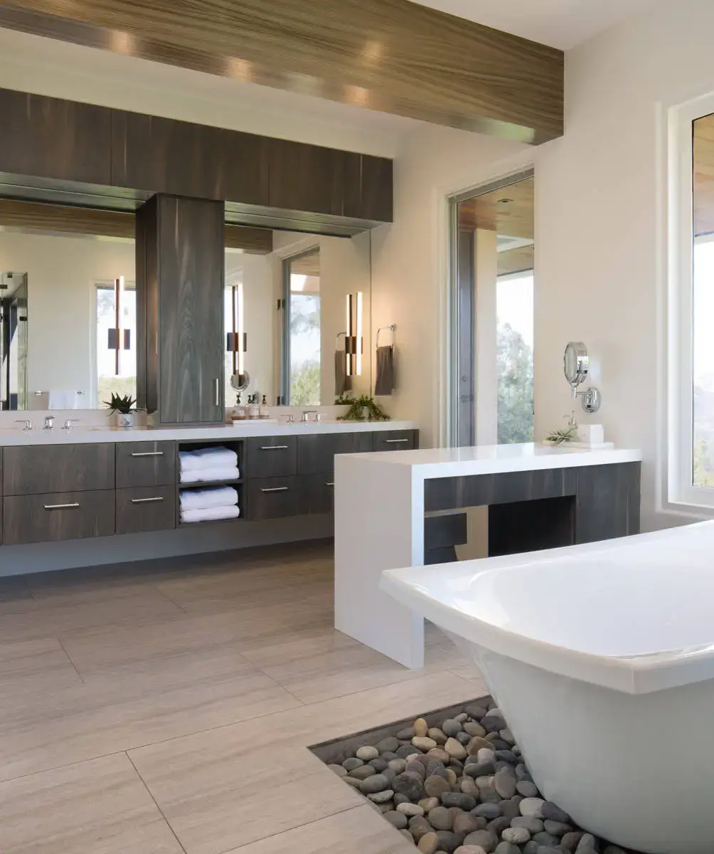 Luxurious modern bathroom with European-inspired cabinetry, featuring sleek wood cabinets, a large mirror, and a freestanding tub surrounded by decorative pebbles for an elegant interior design solution.